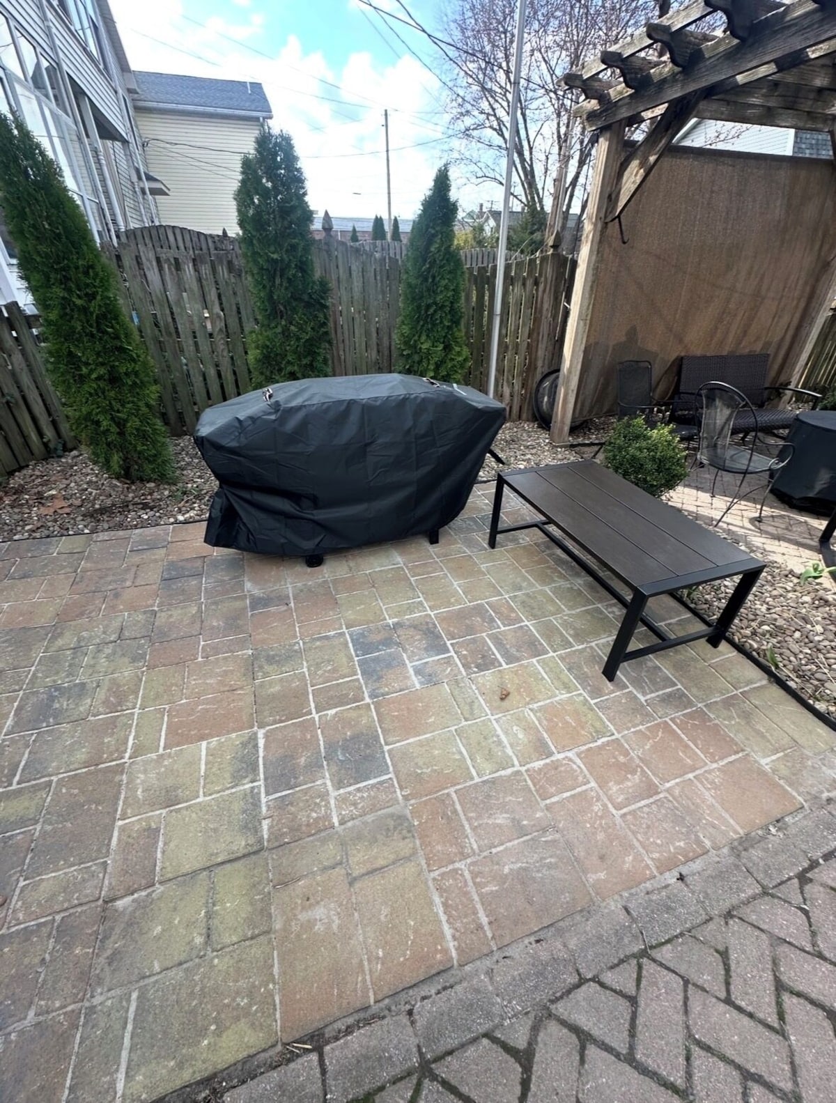 A patio with a covered grill, a bench, and outdoor furniture.