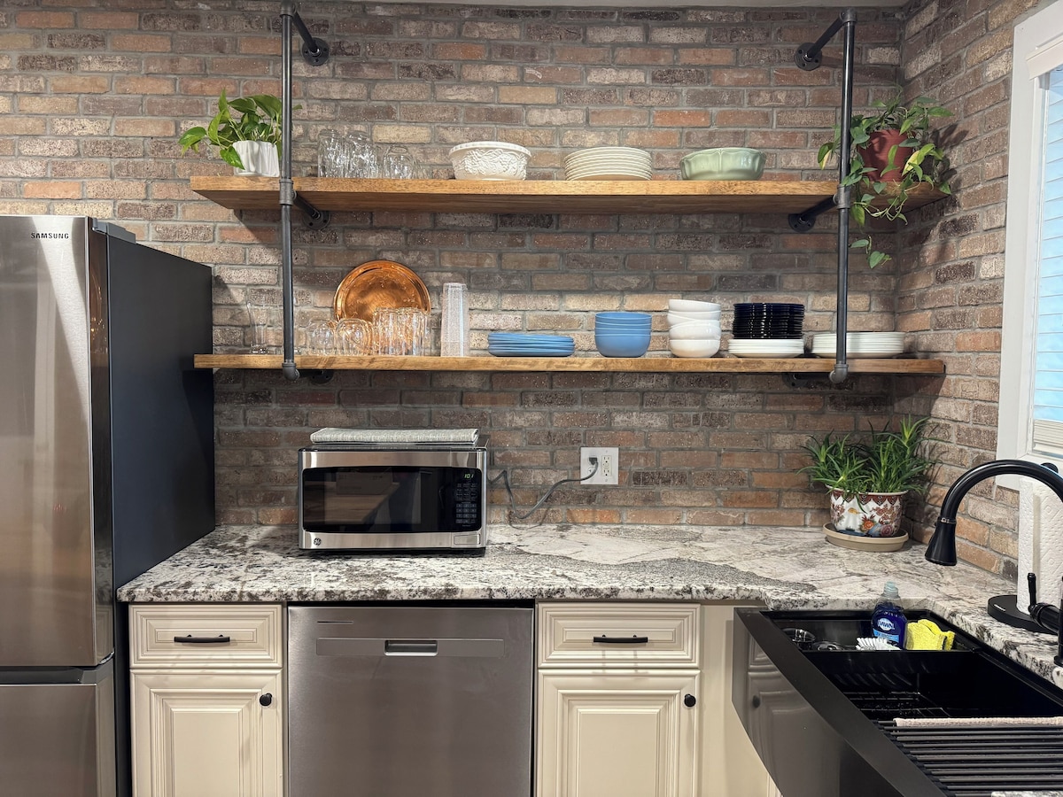 A kitchen with a brick wall, stainless steel appliances, wooden shelves, and potted plants.