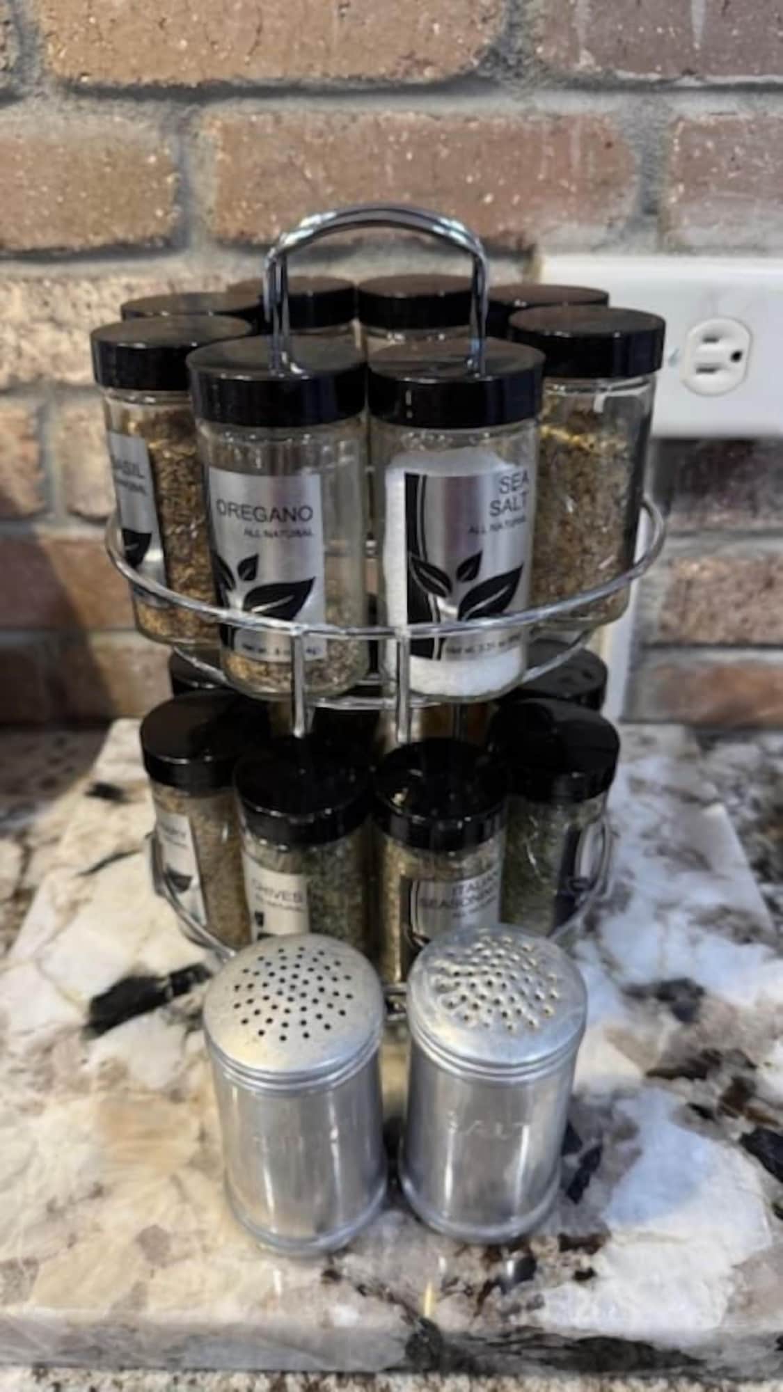 A spice rack with labeled containers and two salt shakers on a kitchen counter.