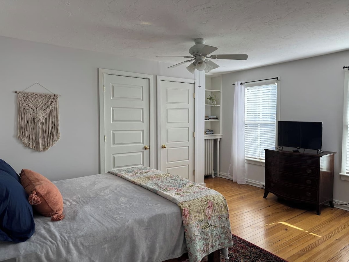 A bedroom with a bed, a dresser, a ceiling fan, and a window with blinds.