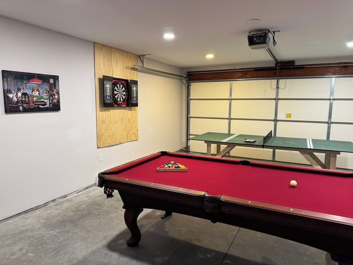 A pool table with a red felt surface, a dartboard, and a framed picture on the wall.