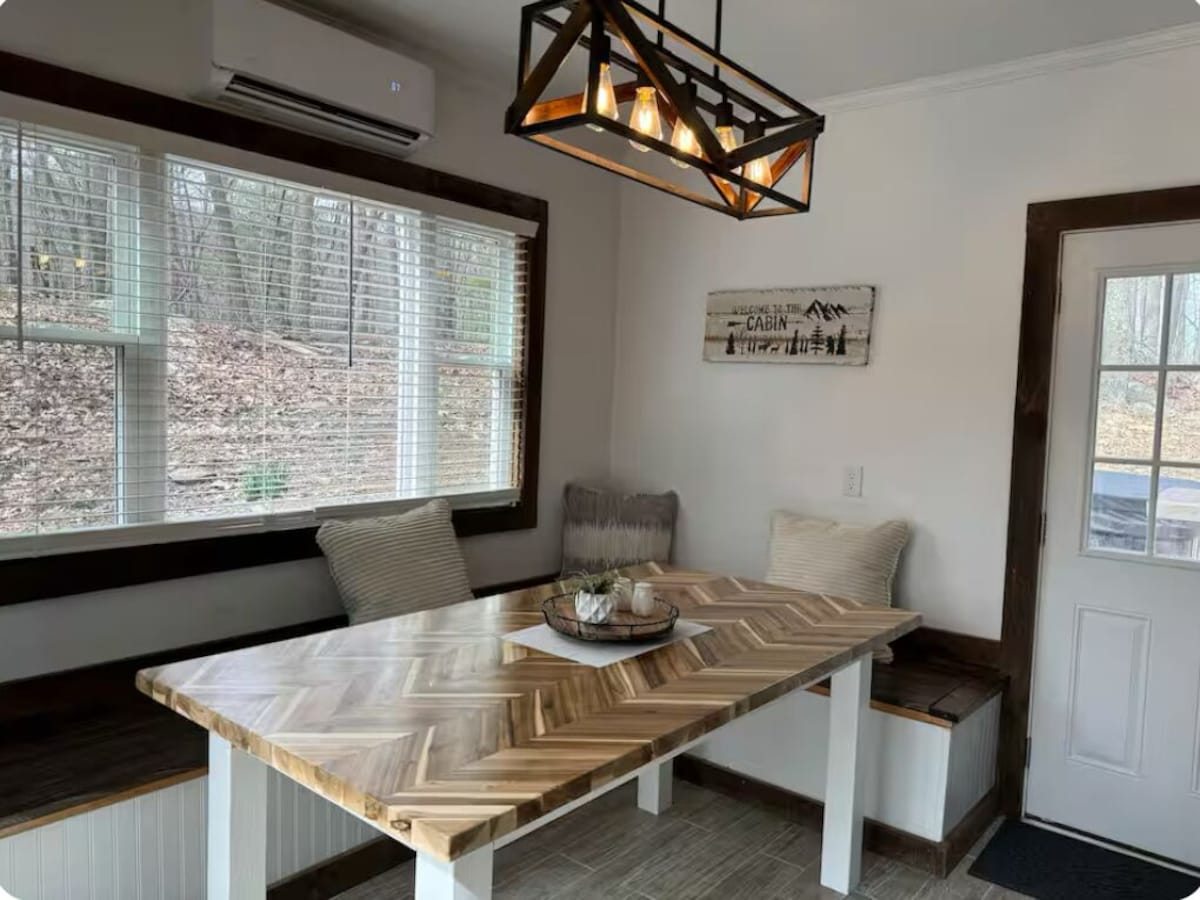 A modern kitchen with a large wooden herringbone table, a built-in bench, and a hanging light fixture.