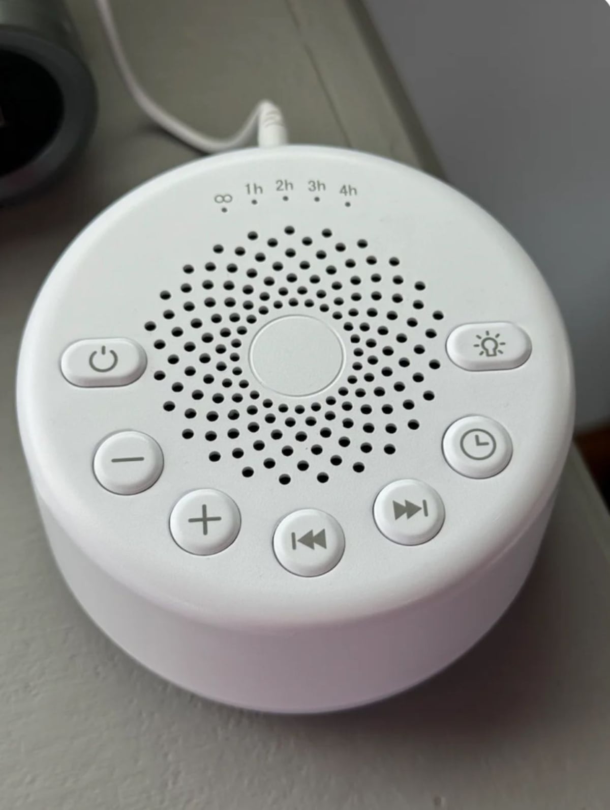 A white, round, portable speaker with a power button, volume control, and play/pause buttons.