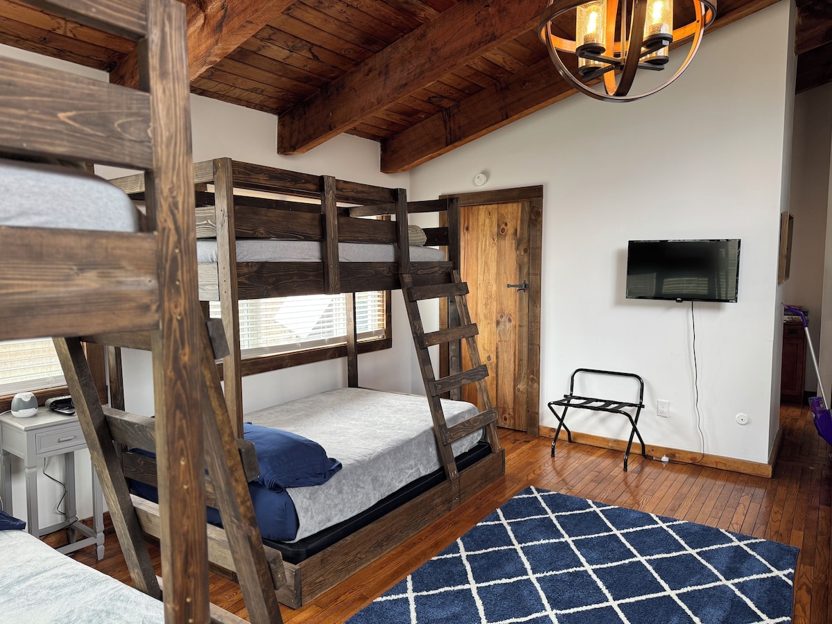 A bunk bed room with wooden beams, a television, and a blue patterned rug.