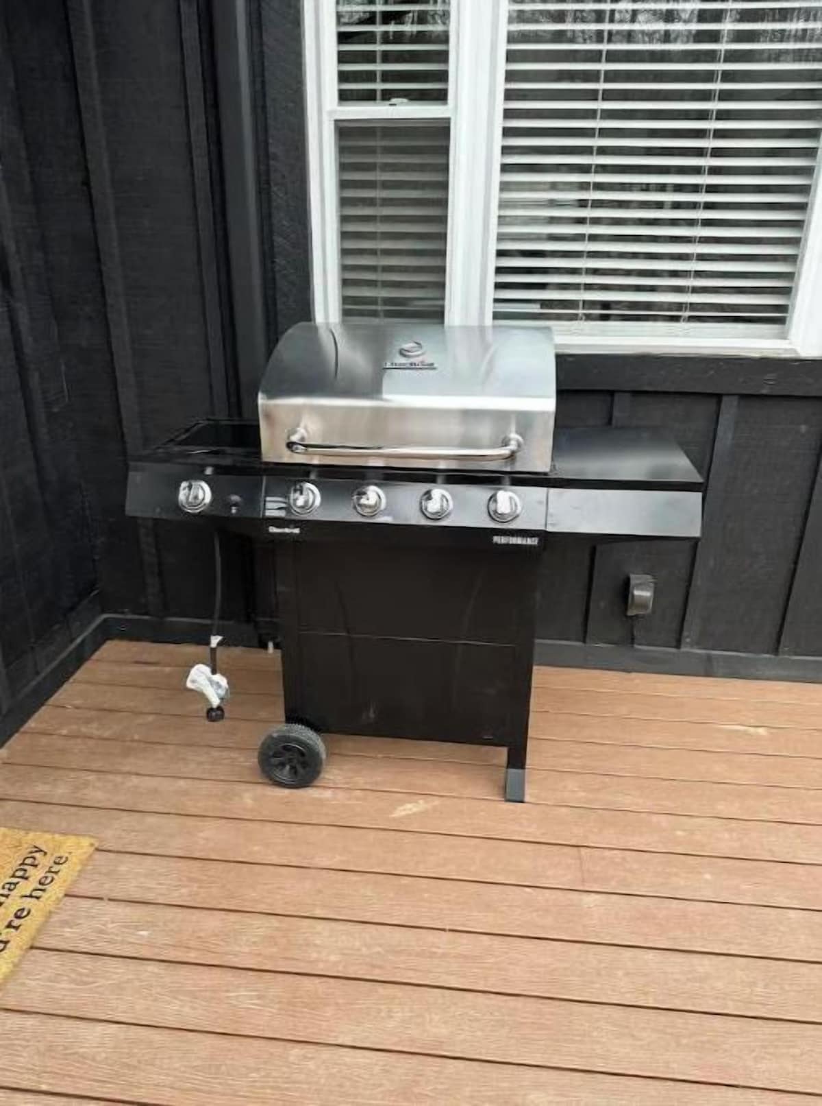 A portable gas grill with four burners and a side burner, placed on a wooden deck.