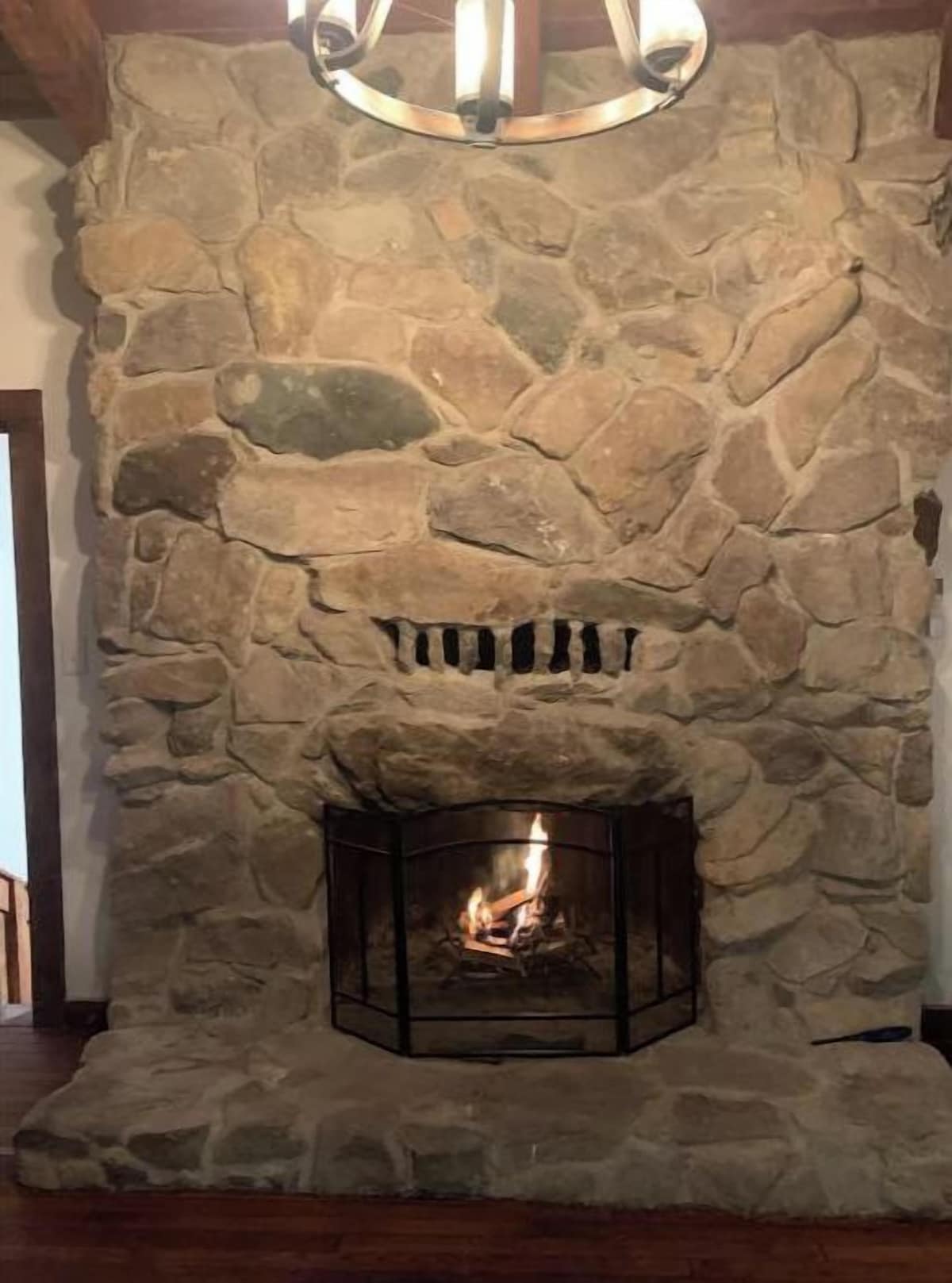 A stone fireplace with a fire burning inside, a wooden mantel, and a stone wall above.
