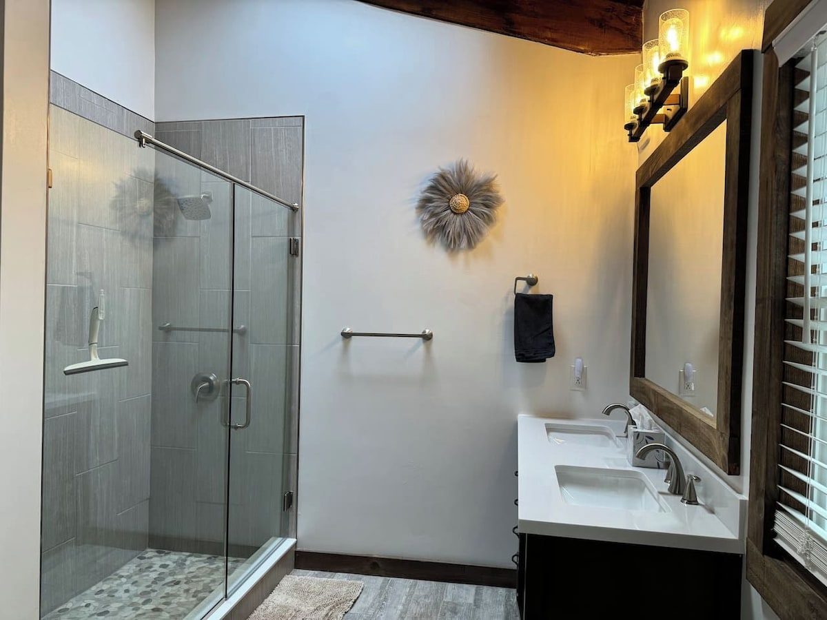A modern bathroom with a glass-enclosed shower, a large mirror, and a white sink.