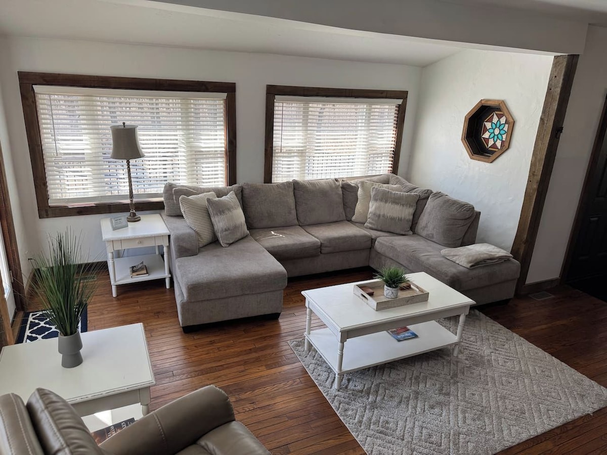 A living room with a sectional sofa, two side tables, a coffee table, and a decorative wall piece.