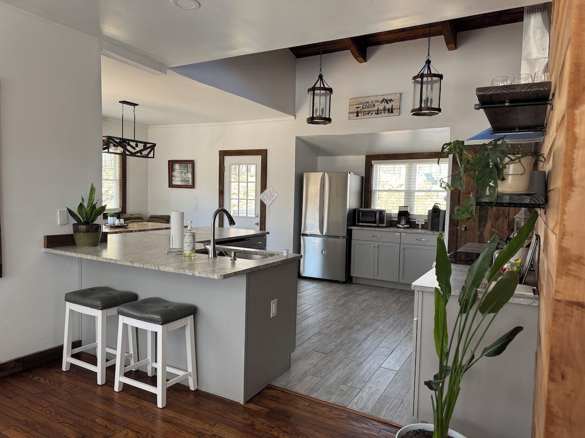 A modern kitchen with a central island, bar stools, stainless steel appliances, and hanging lanterns.