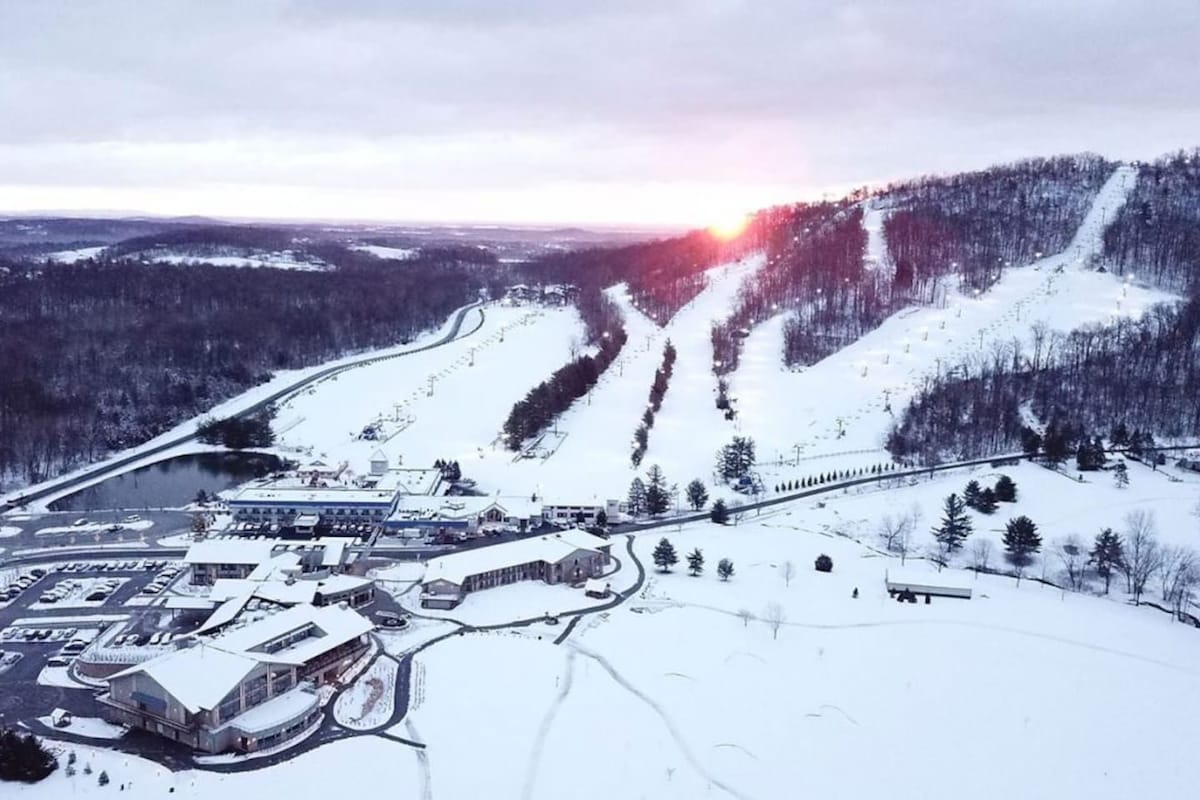 A snow-covered ski resort with a ski lift, buildings, and a winding road.