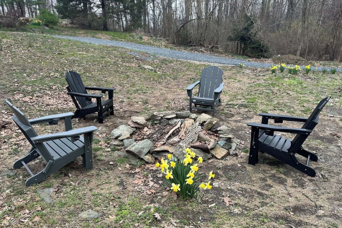 A circular arrangement of Adirondack chairs around a stone fire pit with daffodils in the center.