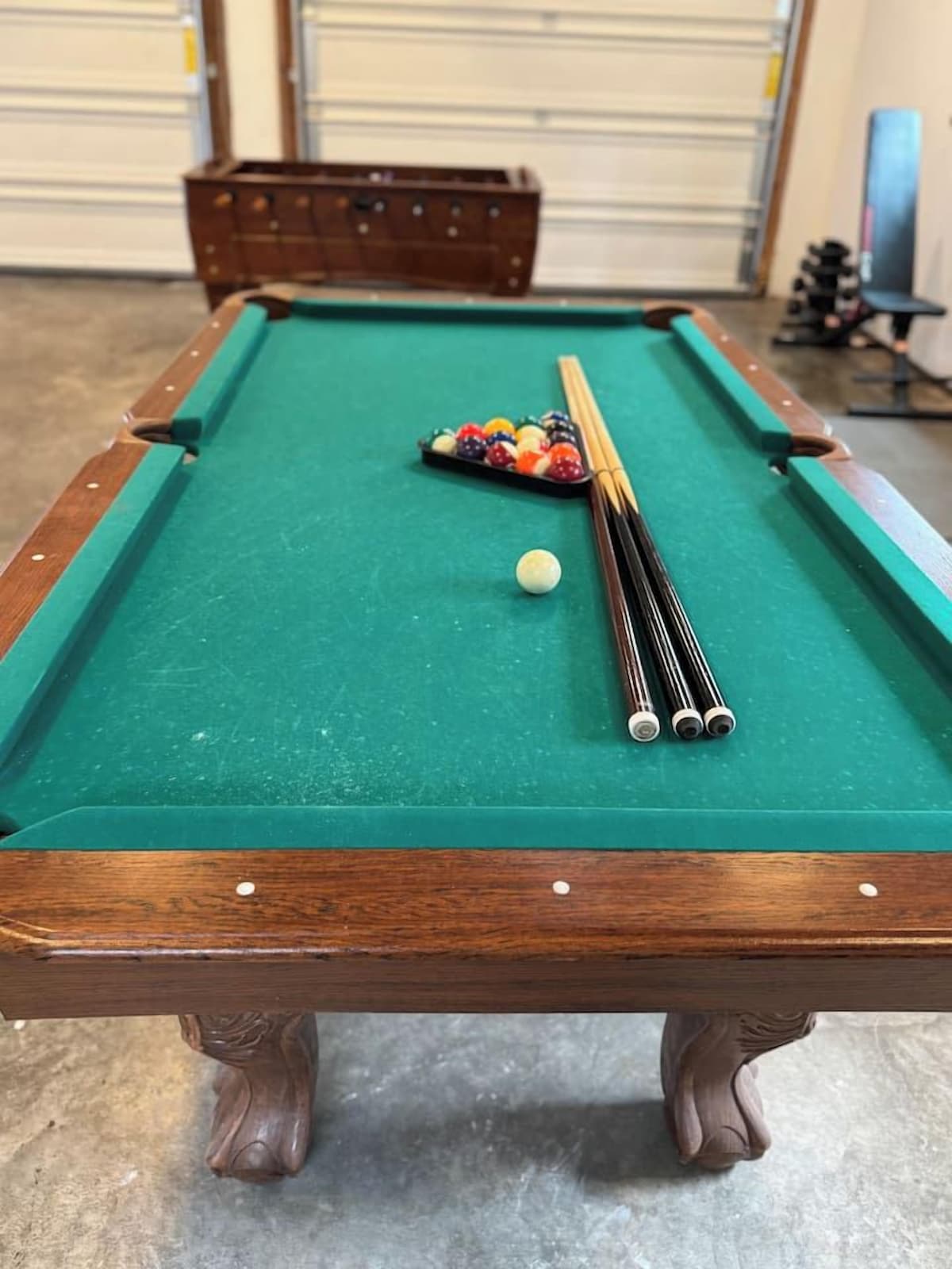 A pool table with a green felt surface, a cue stick, and a set of billiard balls.
