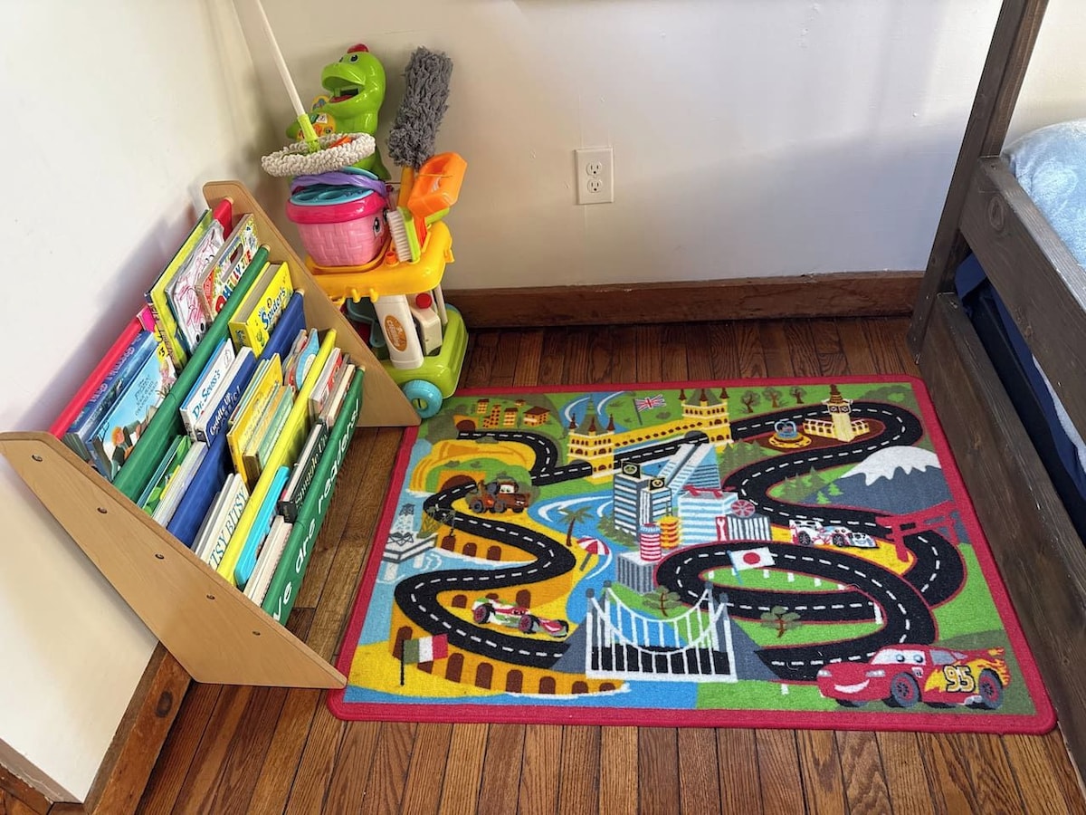 A child's play area with a colorful road mat, a toy car, and a book rack.